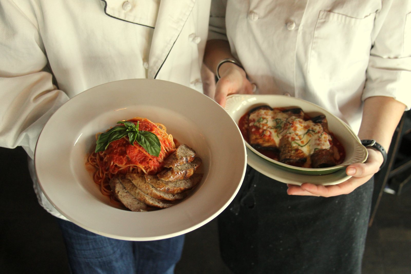 Two servers holding plated pasta dishes ready to carry out