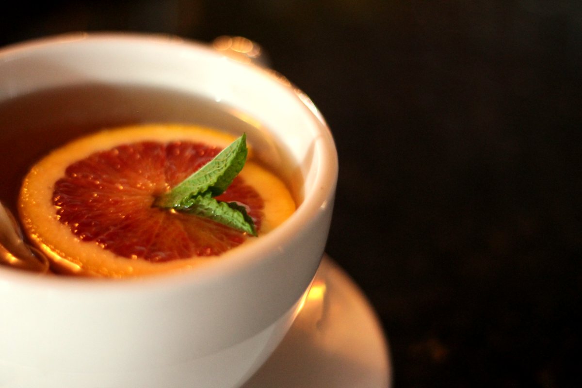 A white cup holding a drink garnished with a dried orange slice and mint