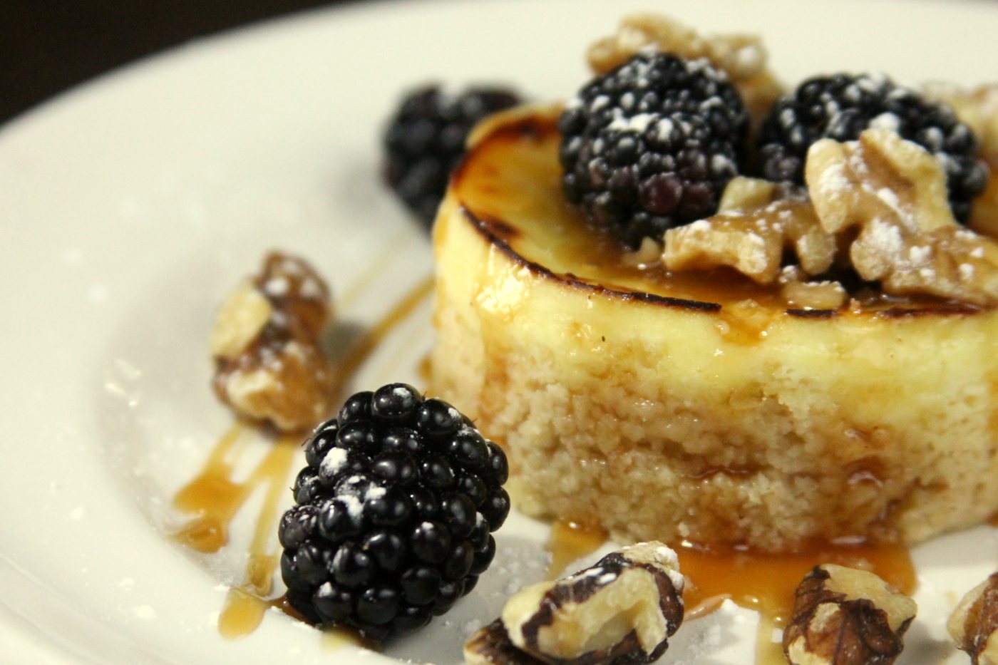 A round dessert topped with blackberries, walnuts and caramel