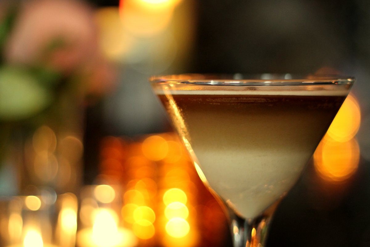A layered cream cocktail in a martini glass in front of candlelight