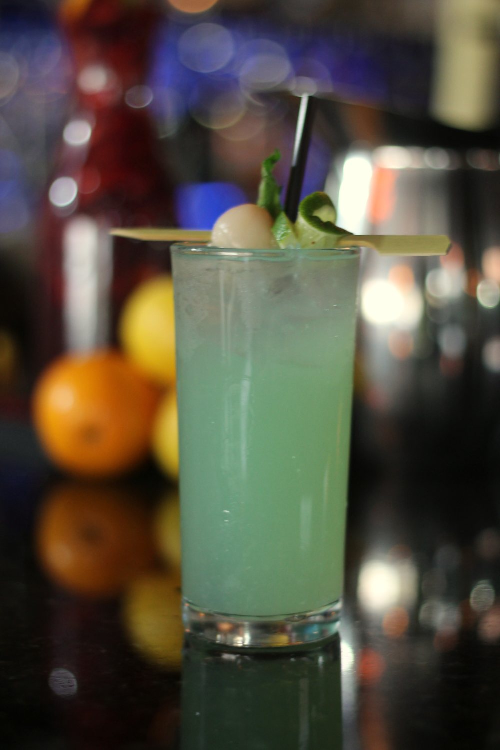 A tall green drink with mint, on the bar in front of the bottles
