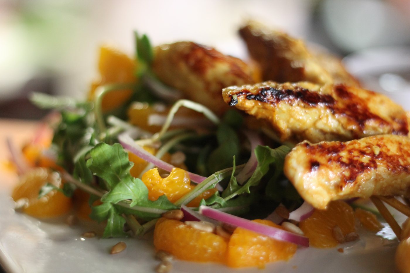 Grilled chicken over a bed of greens with orange segments and red onion